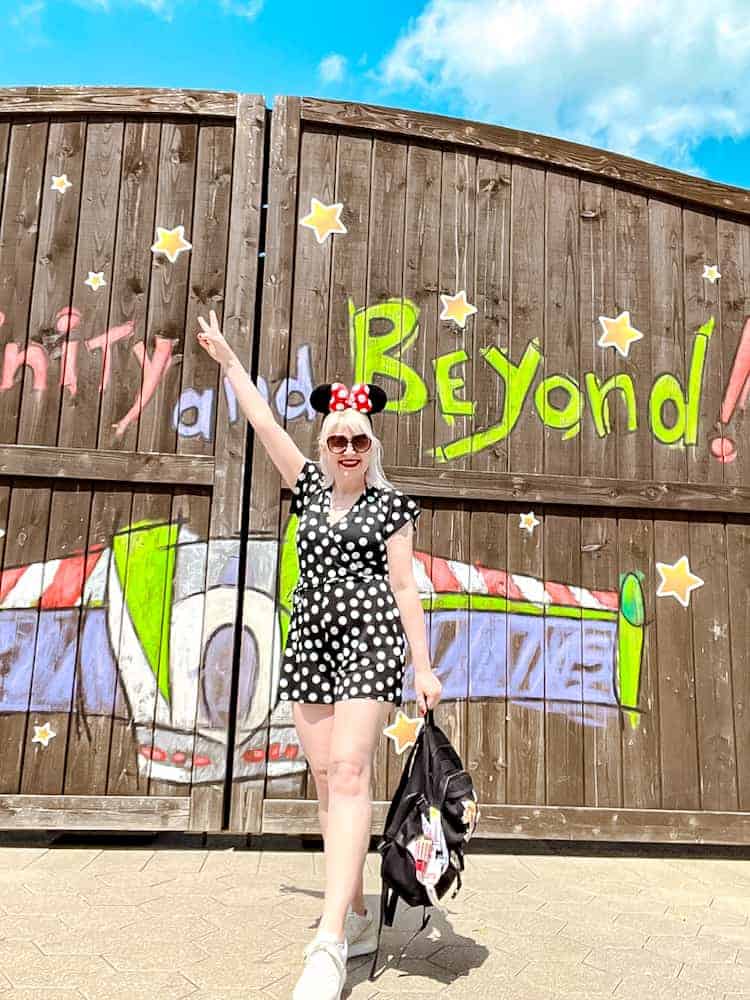 Carrie-Anne poses in a polka dot outfit at a Buzz Lightyear inspired backdrop at Disneyland Paris with blue skies and spring sunshine.