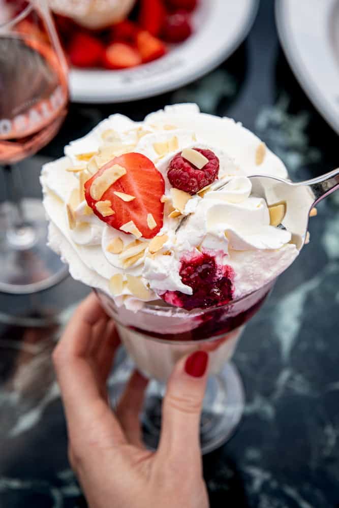 Close-up of a creamy dessert topped with strawberries, raspberries, almonds, and whipped cream at Petite Rosalie in Disney Village