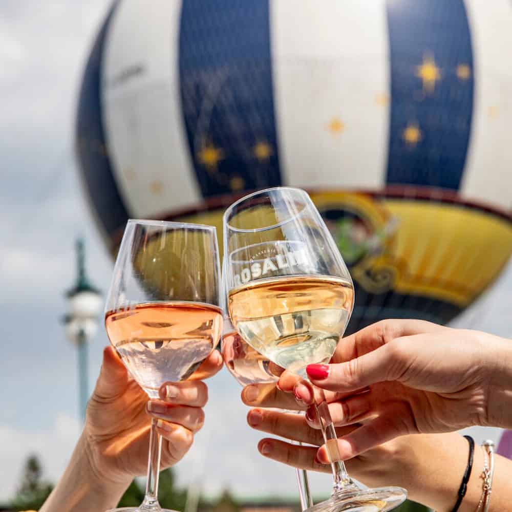 Glasses of rosé and white wine being clinked in front of the PanoraMagique balloon near Petite Rosalie at Disneyland Paris