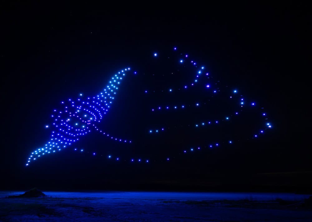 A glowing drone formation shaped like a manta ray floats in the night sky above the lake at Disneyland Paris during tests for the new Adventure Bay night show.