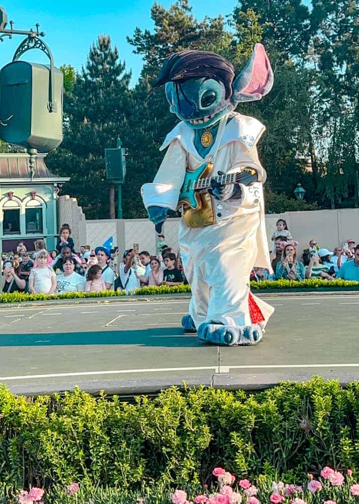 Stitch dressed as Elvis performs onstage with a toy guitar at the Disney Music Festival in Disneyland Paris. A must-see character moment using the virtual queue.