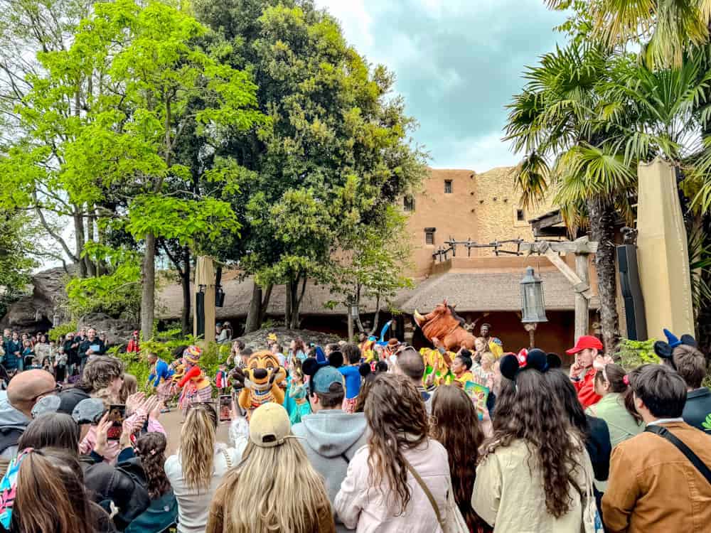 Timon and Pumbaa appear to a large crowd with energetic dancers during their Matadance show at the Disney Music Festival. A crowd gathers to watch this vibrant outdoor performance.
