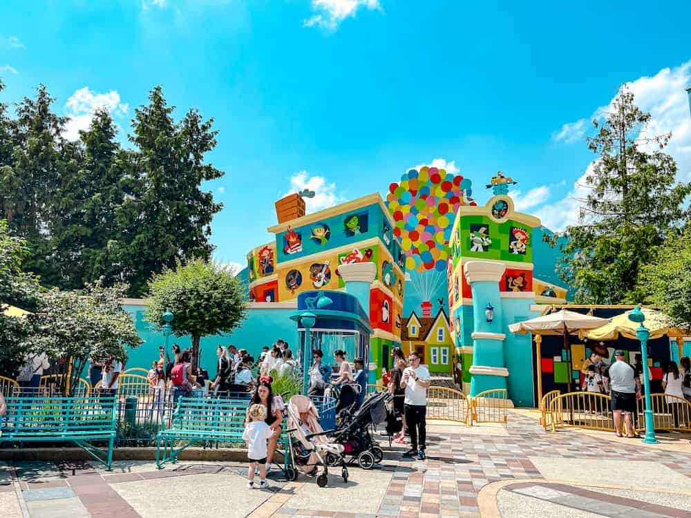 Pushchair parked outside the colourful Pixar-themed meet and greet area at Disneyland Paris, surrounded by families with young children.