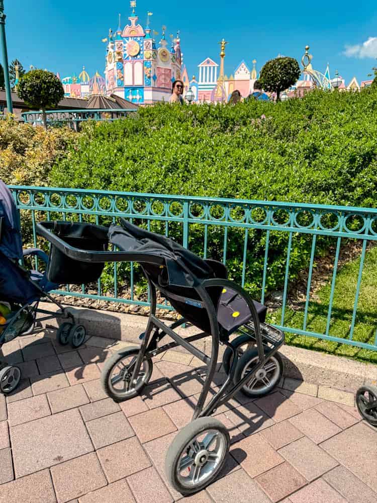 Side profile of Disneyland Paris rental pushchair, showing seat and sunshade design, parked near parade route.