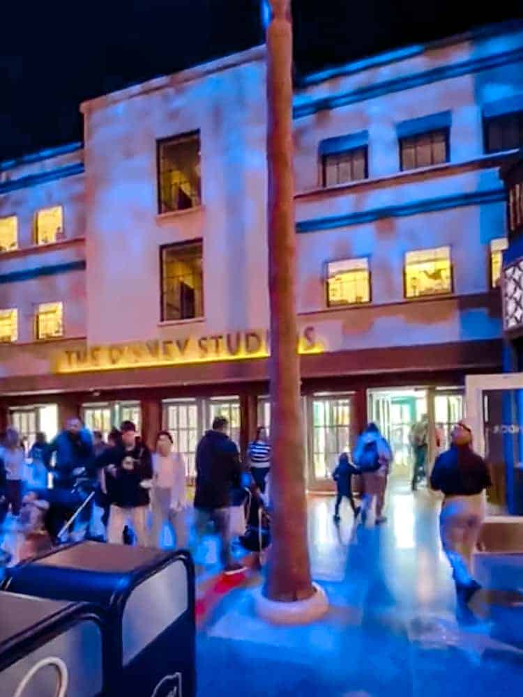 Guests leaving through the back of World Premiere Disneyland Paris, past the Burbank-style studio building with glowing windows.