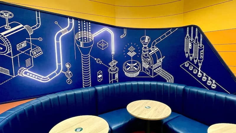 Neon blue coffee machine diagram mural and curved blue booth seating inside the Cars-themed Starbucks at Disneyland Paris.