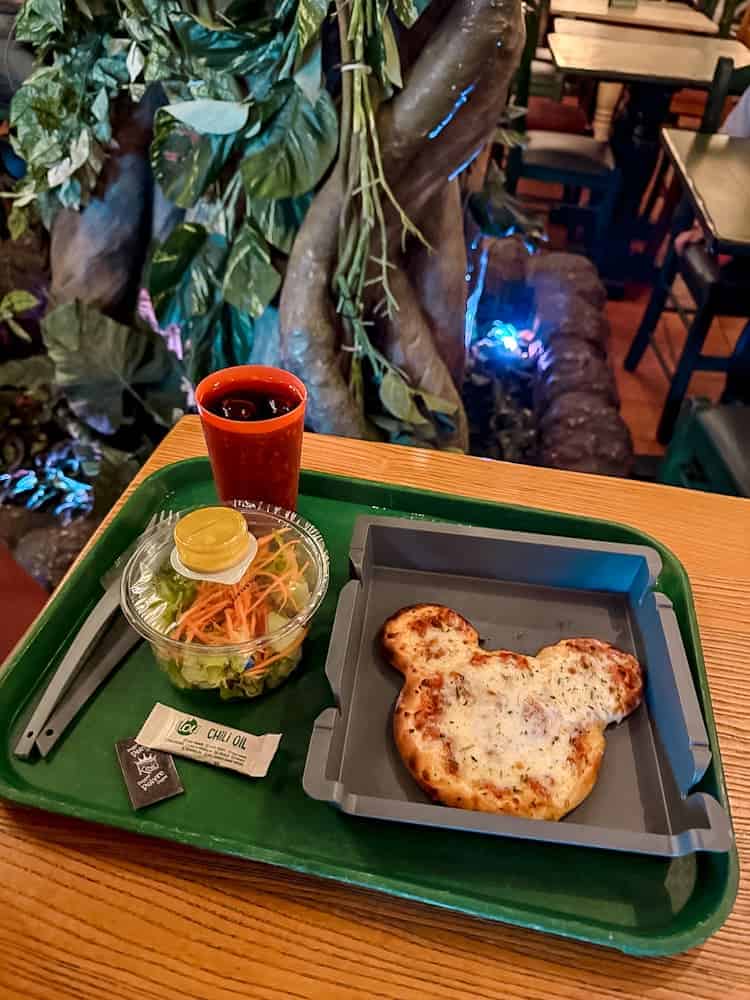 Mickey-shaped pizza with salad and drink on a tray at Colonel Hathi’s – a quick and easy food option when planning your Disneyland Paris trip.