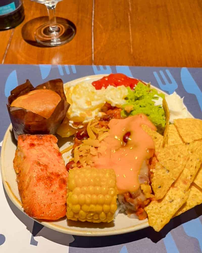 A plate featuring grilled salmon, corn on the cob, veggie chili with cheese, nachos, guacamole, and mashed potatoes from Billy Bob’s buffet.