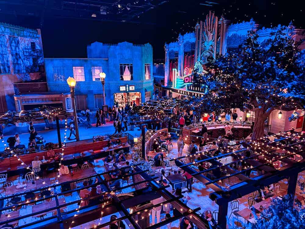 Overhead view of Hollywood Gardens Restaurant at World Premiere Disneyland Paris, with twinkling lights, diners, and the Disney Theater in the background.