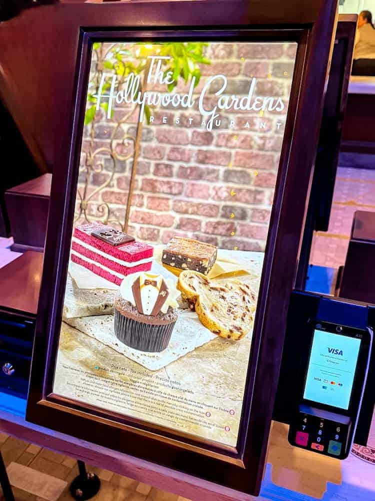 Close-up of dessert display screen at Hollywood Gardens Restaurant in World Premiere Disneyland Paris, featuring red velvet cake and a tuxedo cupcake.