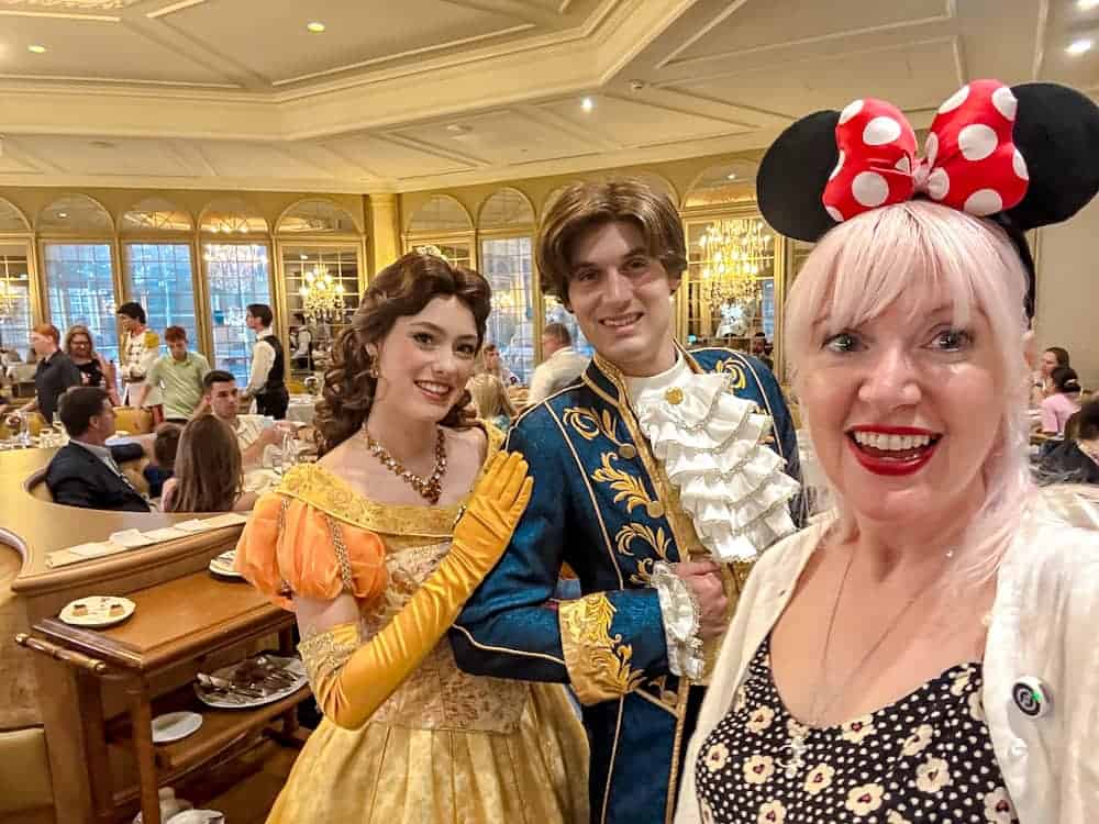 Carrie-Anne smiling with Belle and her prince at La Table de Lumière in Disneyland Paris during a royal character dining experience.