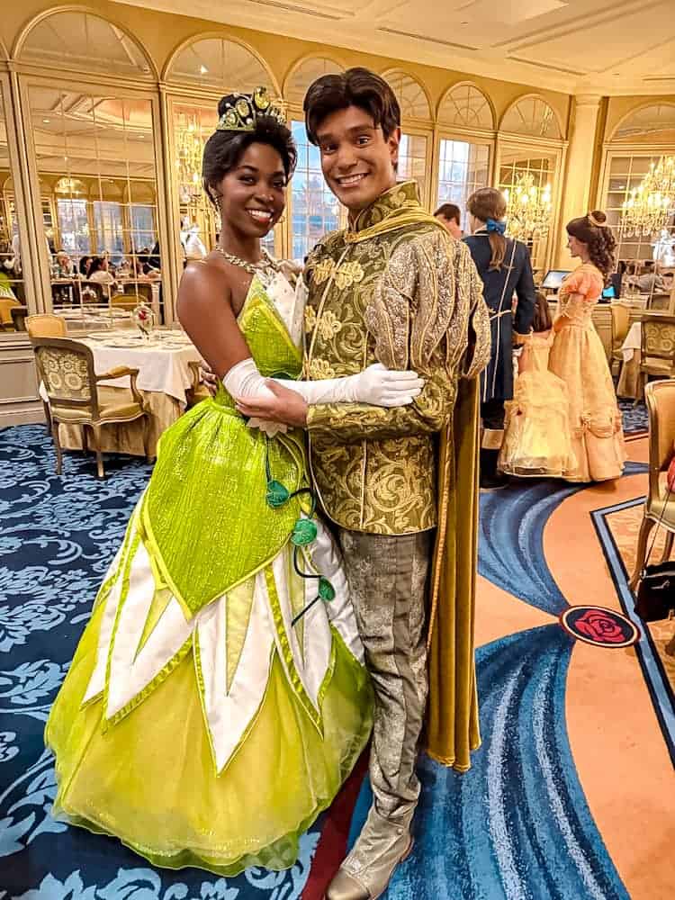Princess Tiana and Prince Naveen smiling together inside the golden ballroom of La Table de Lumière at Disneyland Paris.
