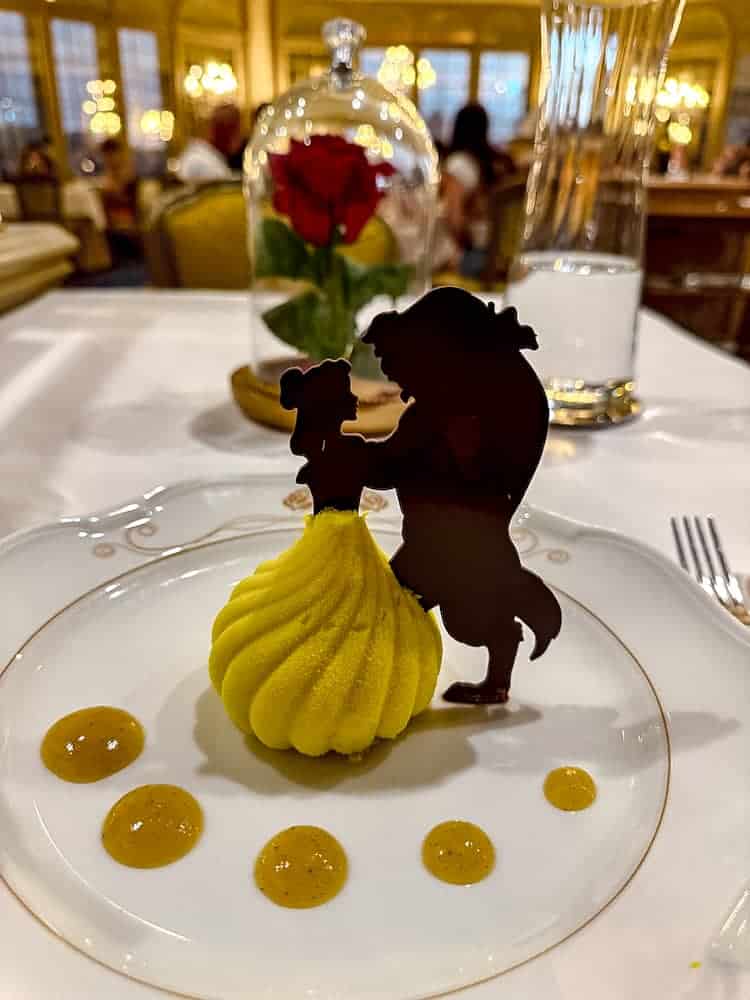 A yellow mousse dessert shaped like Belle’s dress with a chocolate silhouette of Belle and Beast, served at La Table de Lumière, Disneyland Paris.