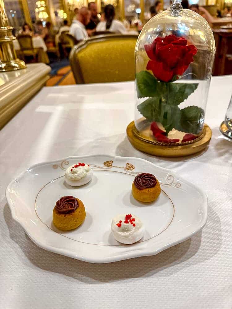 A plate of petit fours served at La Table de Lumière in Disneyland Paris, next to the iconic rose in a dome centrepiece.