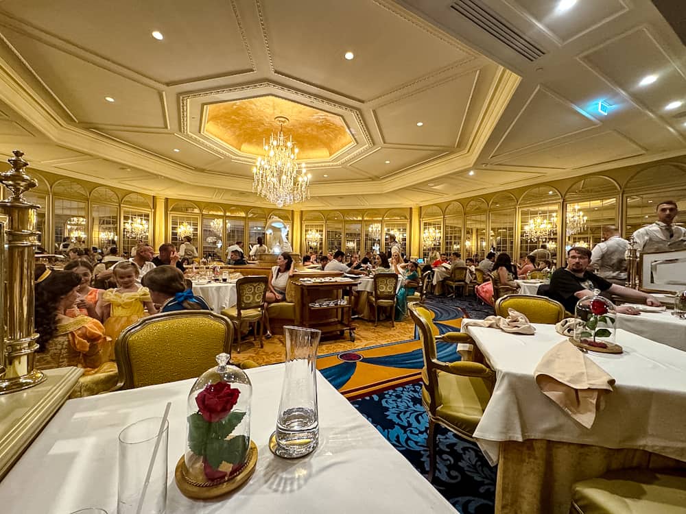 A wide view of the elegant dining room at La Table de Lumière, Disneyland Paris, with families and children dining under sparkling chandeliers.