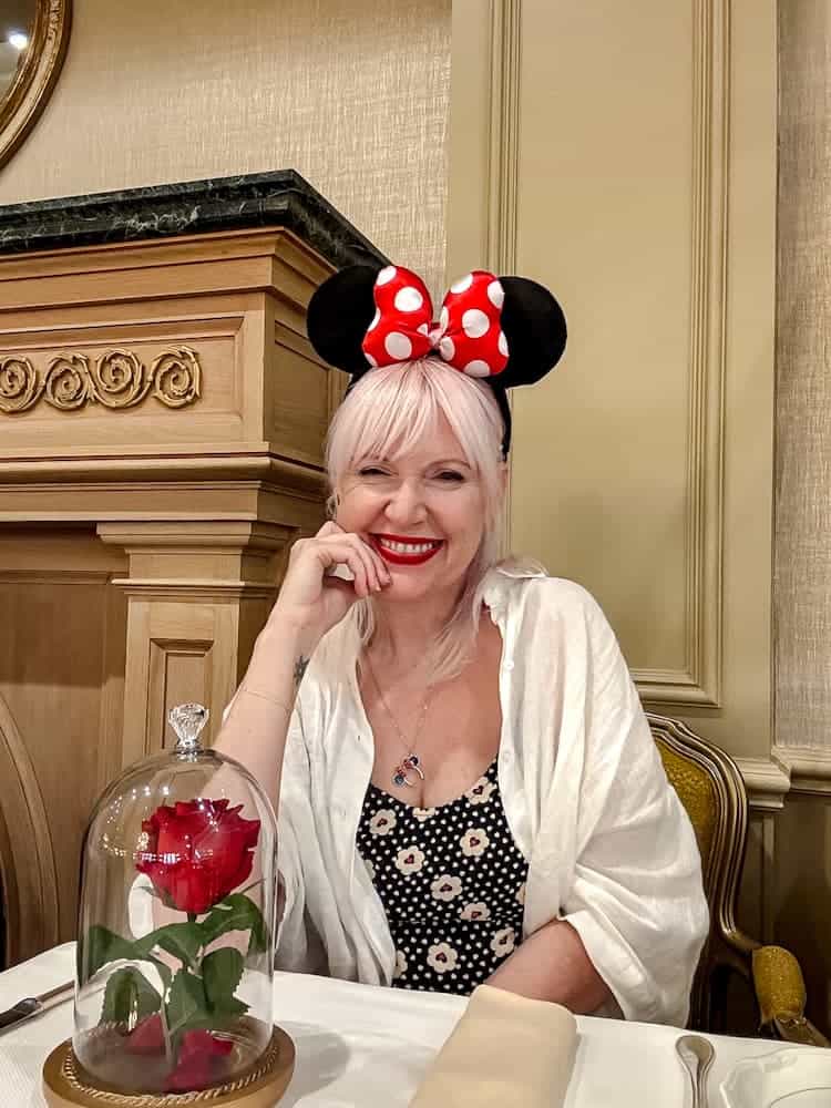 Disneyland Paris blogger Carrie-Anne smiling at her table with the enchanted rose at La Table de Lumière, Disneyland Paris, wearing Minnie ears and a spotty playsuit.