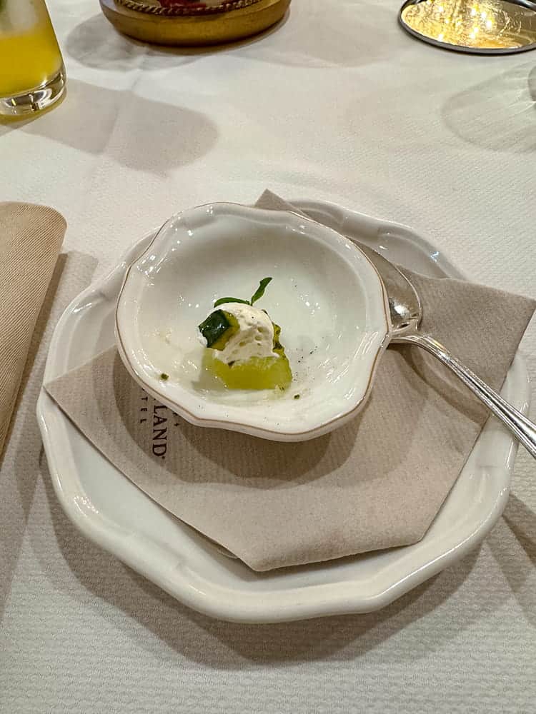 A tiny cucumber amuse-bouche on a white dish, part of the fine dining experience at La Table de Lumière in Disneyland Paris.