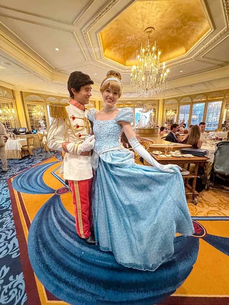 Cinderella and Prince Charming posing under chandeliers at La Table de Lumière, Disneyland Paris character dining experience.