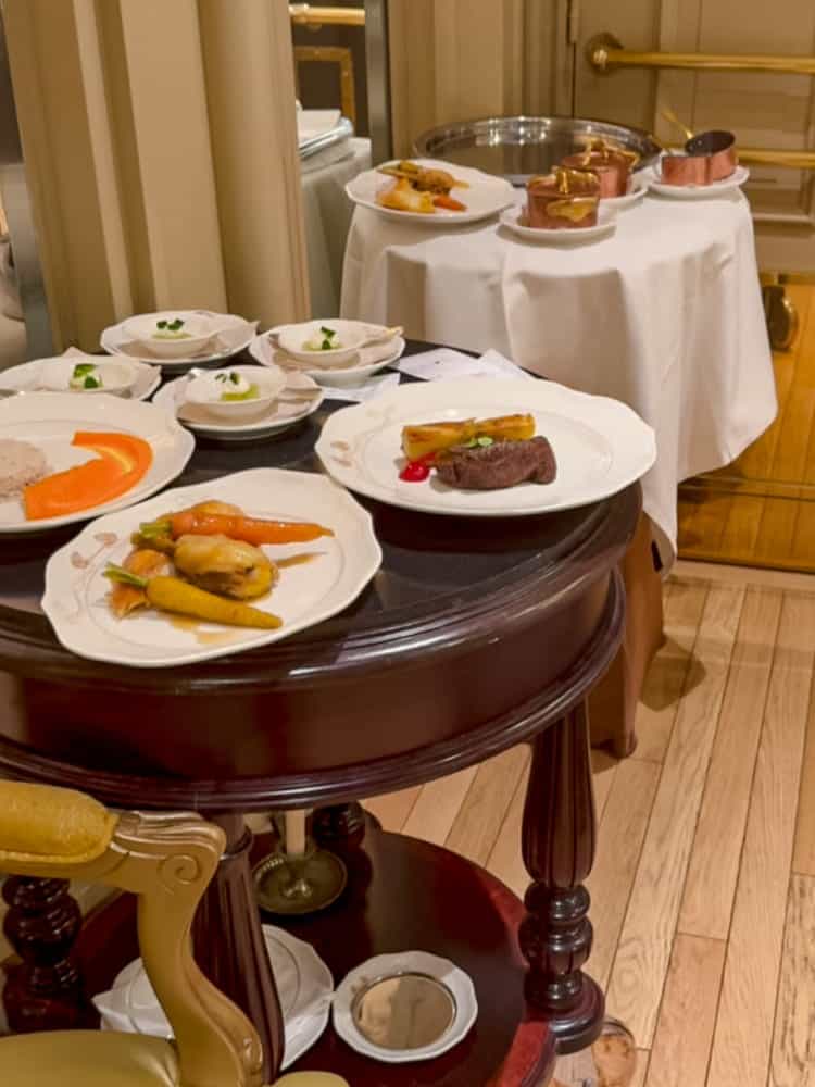 A serving trolley at La Table de Lumière with multiple plated dishes, including carrots, beef, and vegetable accompaniments, ready to be served in the dining room.