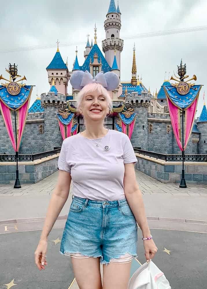 Carrie-Anne in front of Sleeping Beauty Castle at Disneyland California, reflecting on her return visit while comparing Disneyland California vs Disneyland Paris.