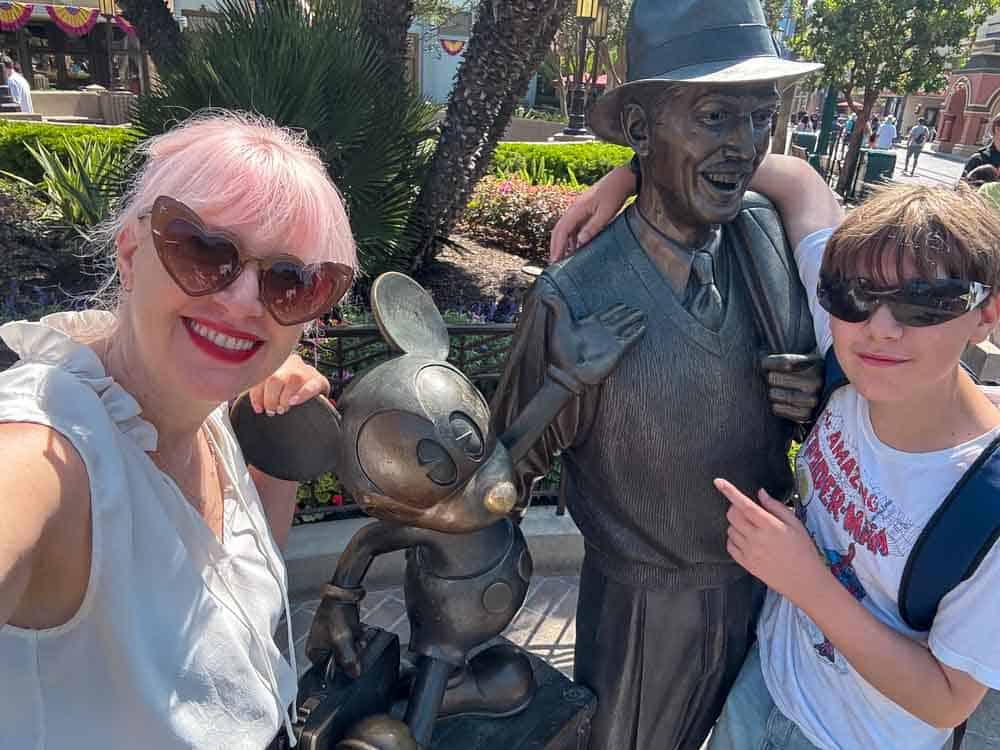 Mother and son posing with the bronze statue of Walt Disney and Mickey Mouse in Disney California Adventure.