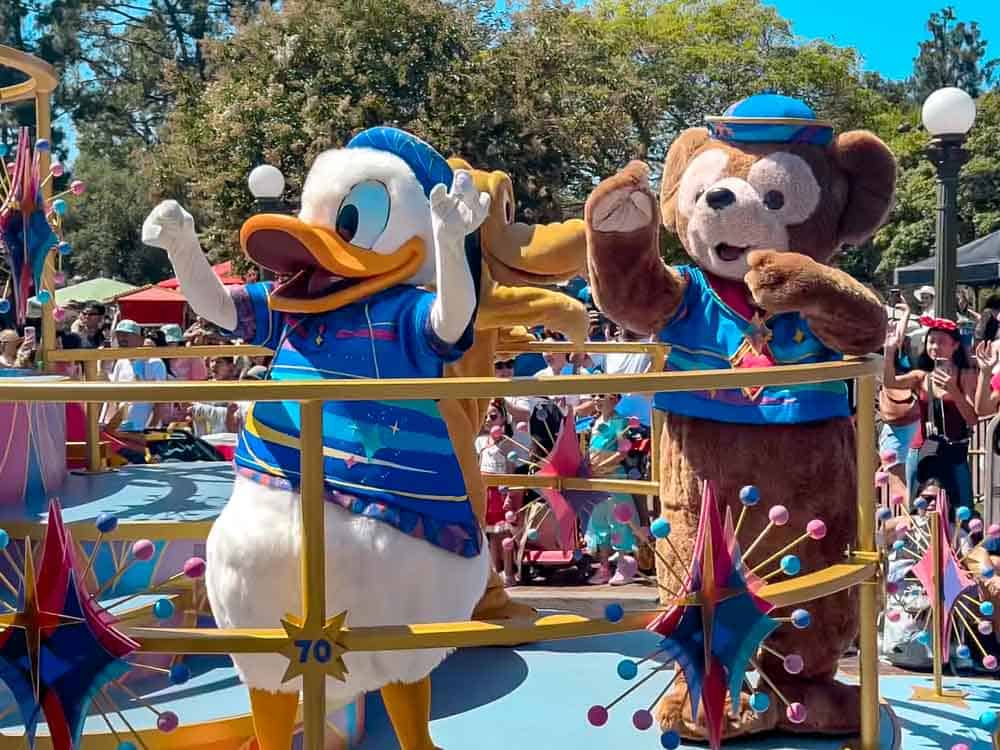 Donald Duck and Duffy the Disney Bear waving from a colourful Celebrate! Happy Parade float at Disneyland California.