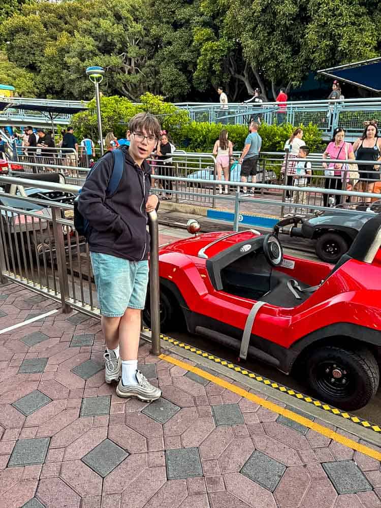 Jackson standing by a red Autopia car, ready to drive, as part of Carrie-Anne’s 3-Day Disneyland California Itinerary in Disneyland Park.