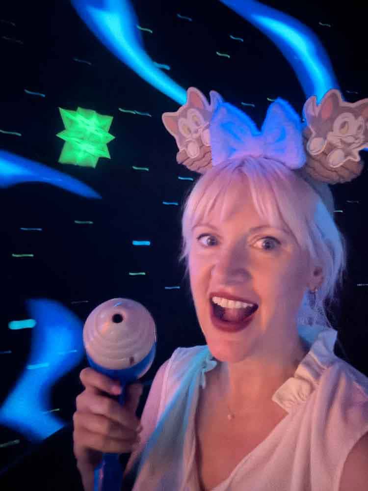 Disney blogger Carrie-Anne wearing Chip and Dale ears smiling with a blaster in hand on Buzz Lightyear Astro Blasters at Disneyland California.