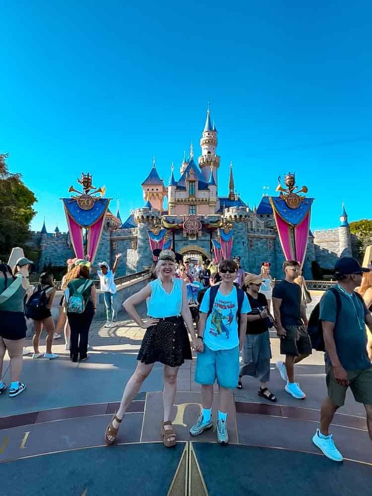 Mother and son posing happily in front of Sleeping Beauty Castle decorated for Disneyland California’s 70th anniversary.