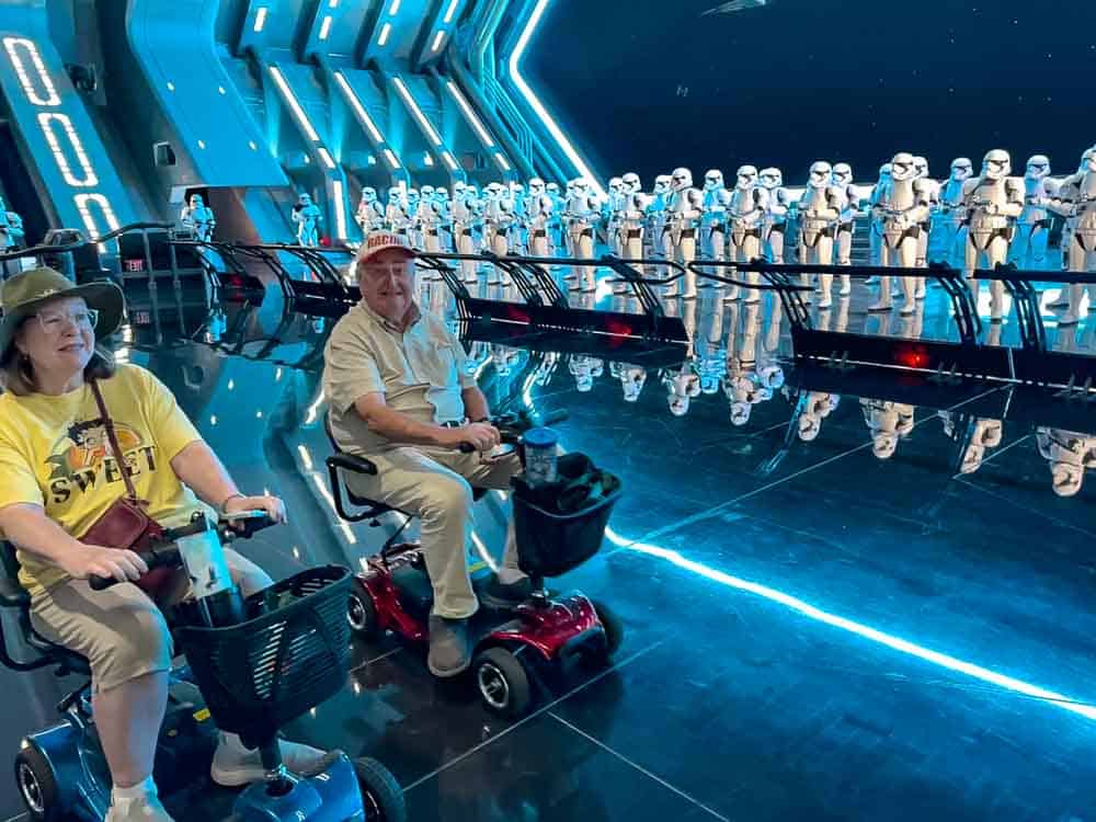 Two elderly guests on mobility scooters enjoy the inside of Rise of the Resistance with a full line of Stormtroopers, part of our 3-Day Disneyland California Itinerary.
