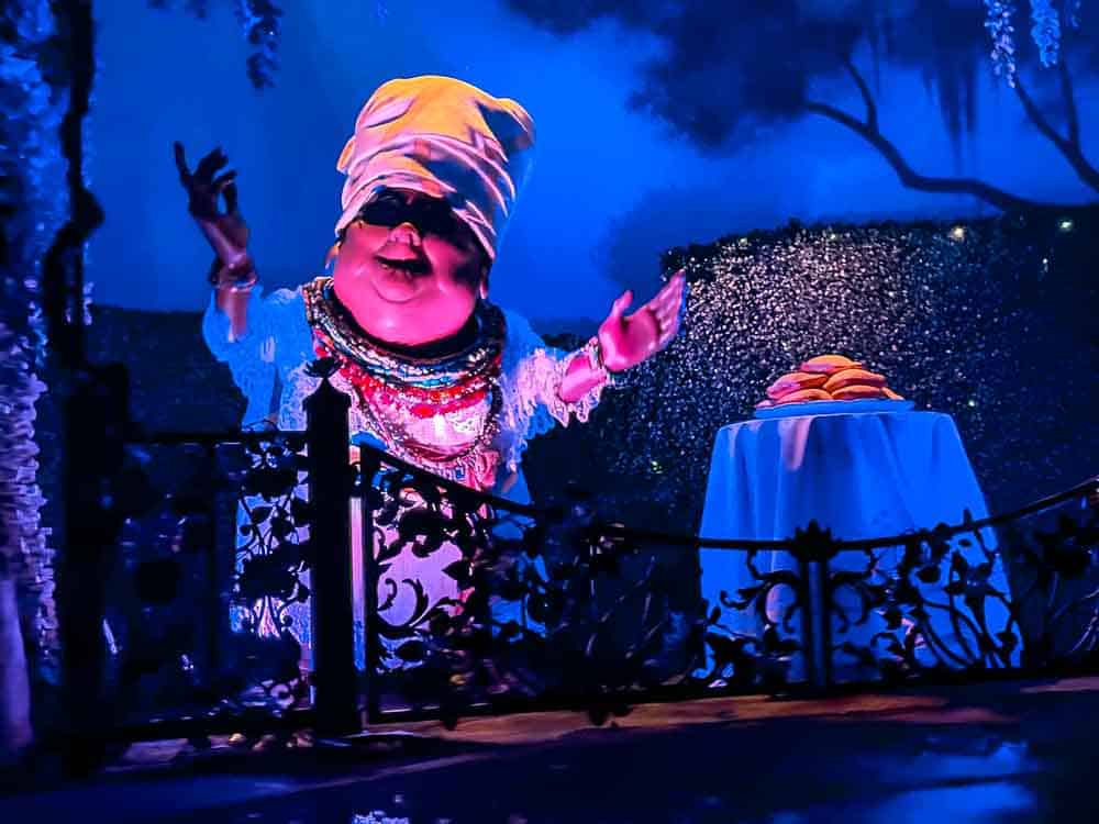 Colourful animatronic chef in a sparkling outfit with a table of beignets inside Tiana’s Bayou Adventure at Disneyland California.