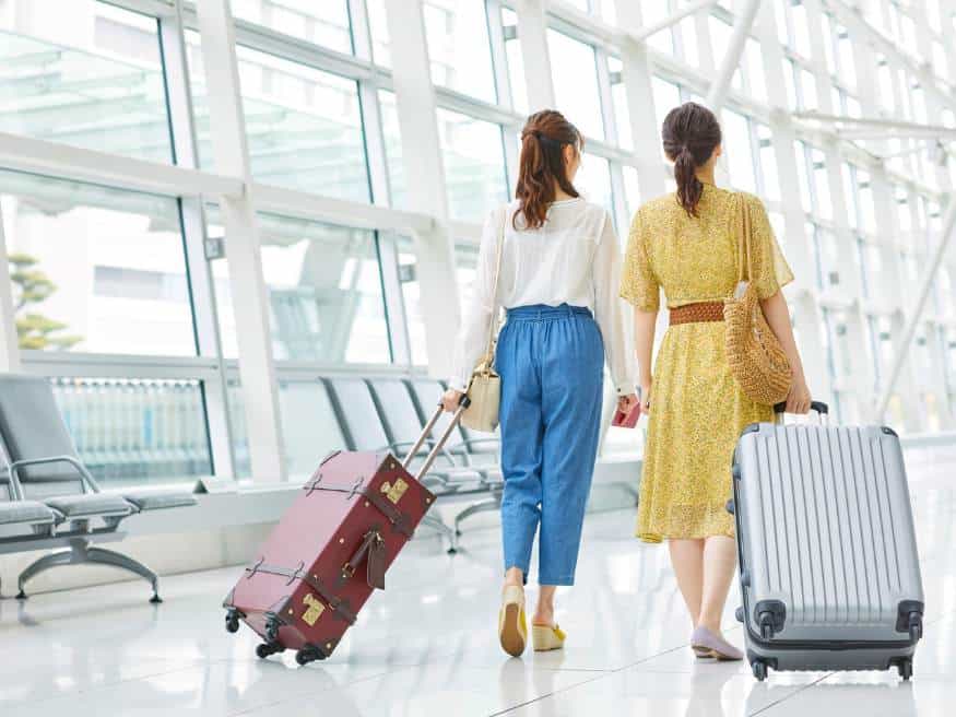 Two women walking with suitcases through a bright airport terminal, representing new Disneyland Paris border checks under the EU Entry/Exit System (EES).