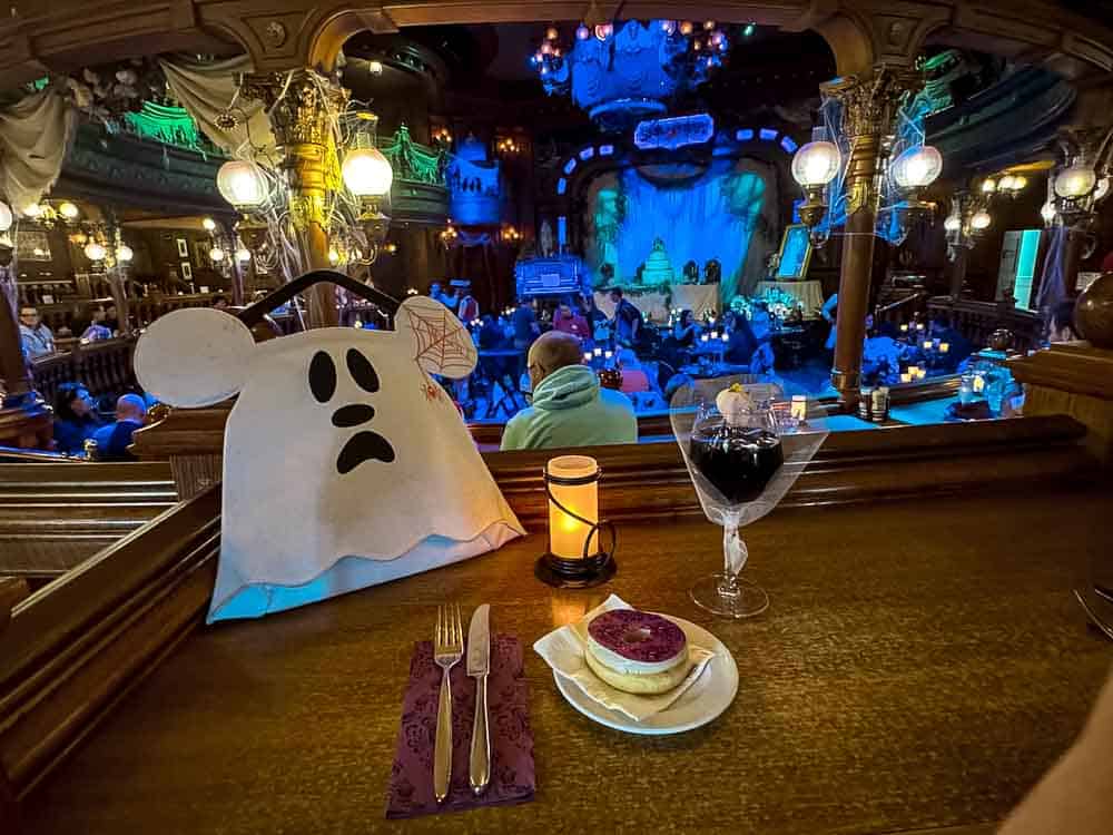 Mélancholique cocktail and Phantom Manor donut on a bar table overlooking the stage inside the Unlucky Nugget Saloon at Disneyland Paris Halloween 2025.
