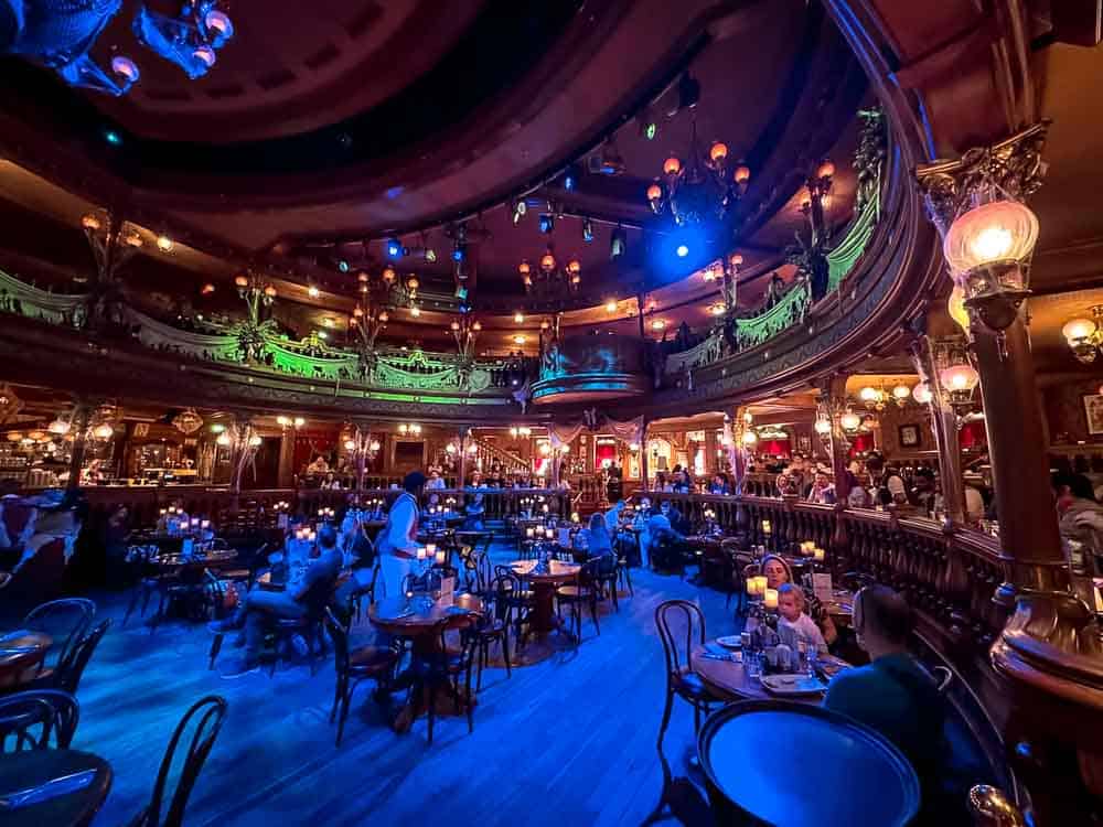 Wide interior of the Unlucky Nugget Saloon showing two-tier dining and glowing chandeliers during Disneyland Paris Halloween 2025.