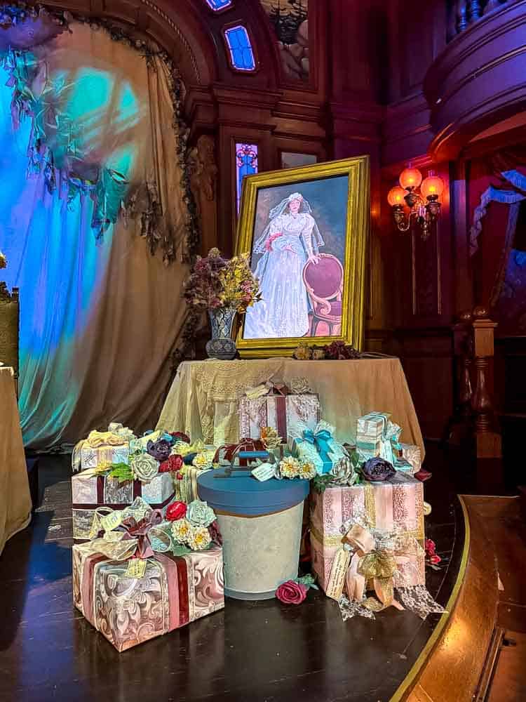 Close-up of Melanie Ravenswood’s portrait and unopened wedding gifts surrounded by flowers inside the Unlucky Nugget Saloon at Disneyland Paris Halloween 2025.