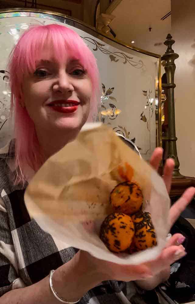 Disneyland Paris blogger Carrie-Anne holding a bag of five orange-glazed Halloween donuts from Cable Car Bakery at Disneyland Paris
