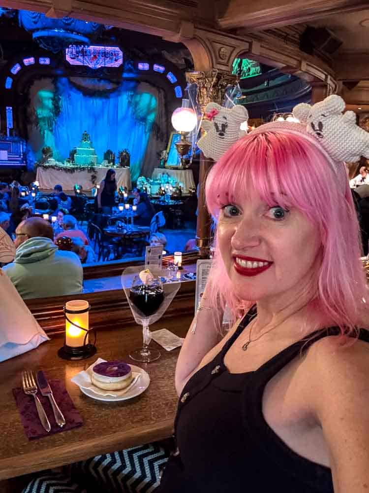 Carrie-Anne sitting at a table inside the Unlucky Nugget Saloon surrounded by Halloween theming