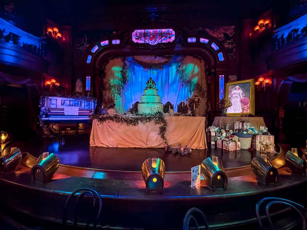 Spooky Phantom Manor-themed stage with wedding cake, piano and ghostly props inside the Unlucky Nugget Saloon at Disneyland Paris Halloween 2025