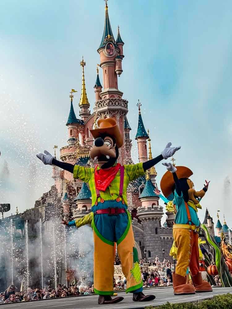 Goofy in colourful Halloween harvest costume performing on stage with Sleeping Beauty Castle, fireworks and fountains in the background at Disneyland Paris Halloween 2025