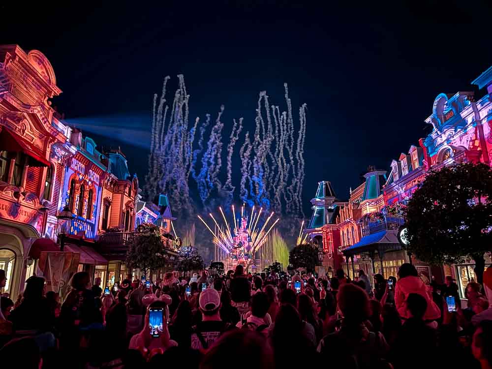 Watching from Main Street USA, colourful fireworks light up the night sky above Sleeping Beauty Castle on a rainy night at Disneyland Paris in the rain.