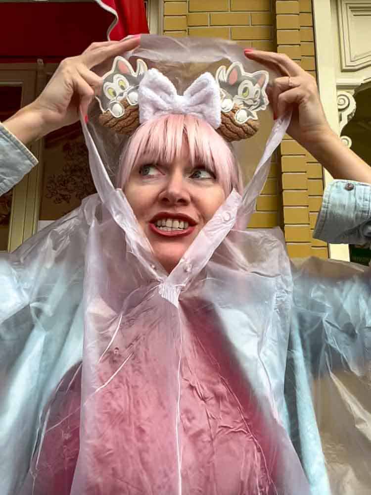 Carrie-Anne smiling under a clear Disneyland Paris poncho, staying dry and cheerful in the rain with her Figaro mouse ears.