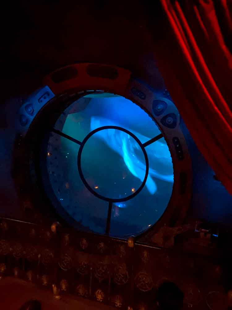 View of a glowing squid outside the porthole during the submarine attack scene in Nautilus – one of the most immersive indoor experiences at Disneyland Paris in the rain.