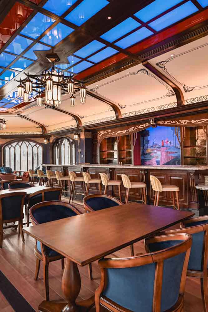 Interior of the Regal View Lounge Disneyland Paris featuring deep blue seating, warm wooden finishes, a long bar and lakeside windows.