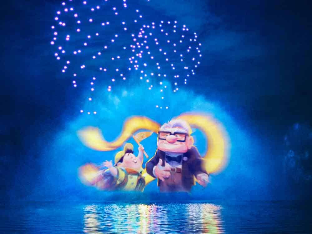 UP characters Carl and Russell illuminated on the water screen with glowing drone formations and colourful fountains during Disney Cascade of Lights at Disneyland Paris.