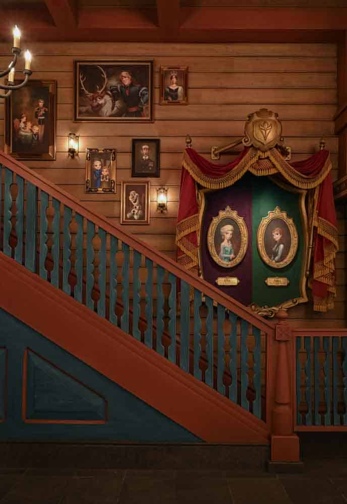 Inside Nordic Crowns Tavern Disneyland Paris, showing the grand staircase and a wall of framed portraits of Anna, Elsa, Kristoff, Sven, Olaf and Arendelle’s royal family, styled in cosy Nordic chalet décor.
