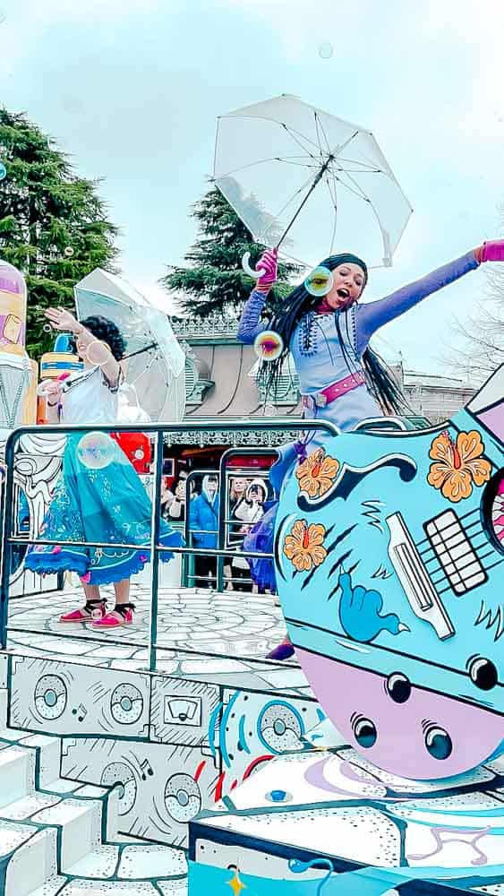 Parade performers (Asha from Wish and Mirabel from Encanto) holding umbrellas and surrounded by bubbles during Million Splashes of Colour - a February parade at Disneyland Paris that happens even in the rain