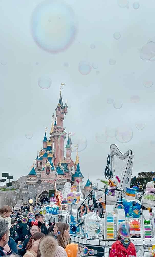 Donald Duck leading a parade through Disneyland Paris in February with bubbles and guests following in front of Sleeping Beauty Castle