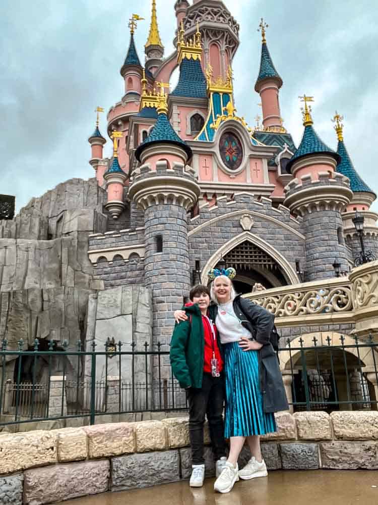 Parent and child posing in front of Sleeping Beauty Castle during a February visit to Disneyland Paris