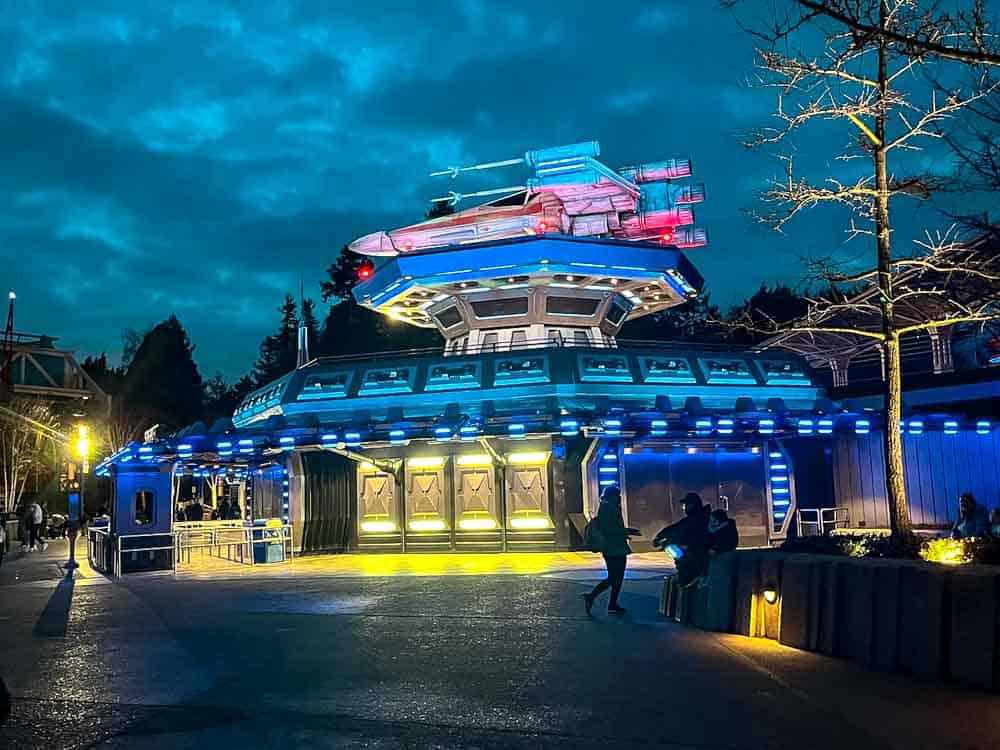 Disneyland Paris at night in February showing winter lighting and calm evening atmosphere; a Star Wars lightspeeder sits on top of a lighted building in Discoveryland
