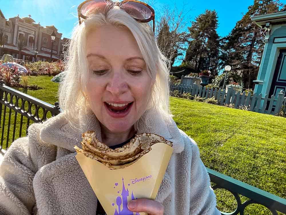 Disneyland Paris blogger Carrie-Anne enjoying a fresh crêpe at Disneyland Paris in February, wrapped up warm on a sunny winter day